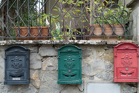 black, green, and red steel mailboxes mounted on gray concrete wall