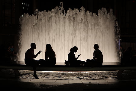 silhouette of four people sitting on bench by the fountain at night