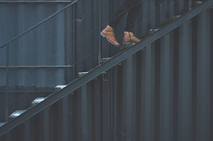 man wearing brown leather boots climbing on black metal stairs at daytime