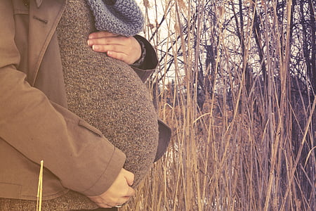 woman holding her baby bump near green grass