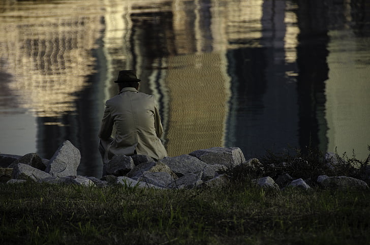 man sitting on grass facing body of water