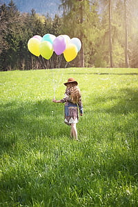 woman holding balloons walking on green grass field