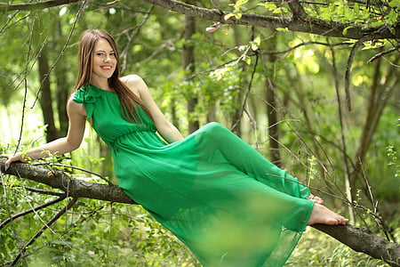 woman wearing green dress sitting on branch during daytime