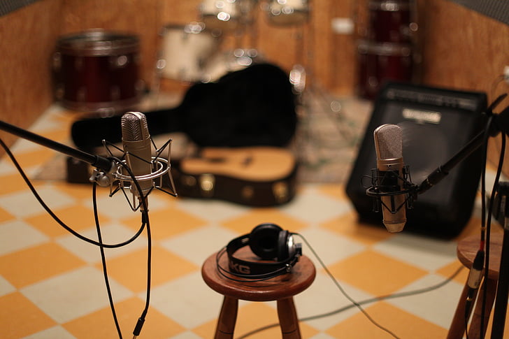 shallow focus photography of black headphones on brown wooden bar stool chair between microphones with stands
