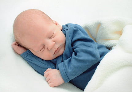 baby wearing dark-blue long-sleeved shirt sleeping on white textile