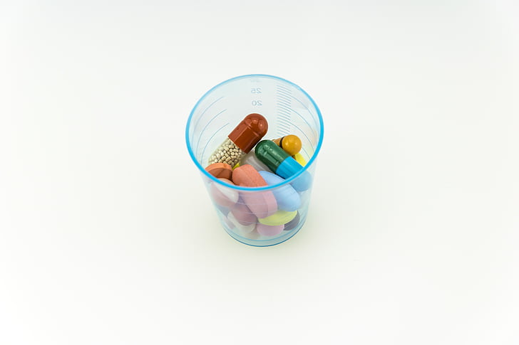 assorted-color capsules and tables on blue plastic cup on white surfacxe