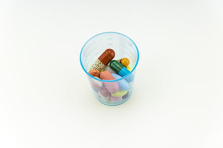 assorted-color capsules and tables on blue plastic cup on white surfacxe