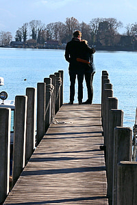 man hand over woman's shoulder standing on dock facing body of water