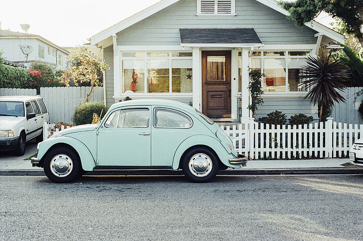 teal Volkswagen Beetle near white wooden house