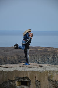 man wearing black jacket carrying woman on hilltop during daytime