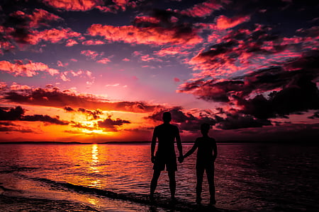 silhouette of man and woman standing on seashore during sunset