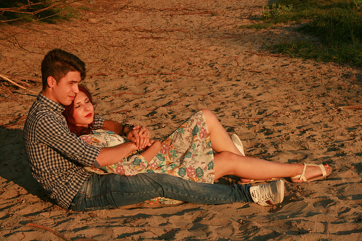 Attractive Couple Flirting On Beach. Girl Sits Between Legs Of Guy