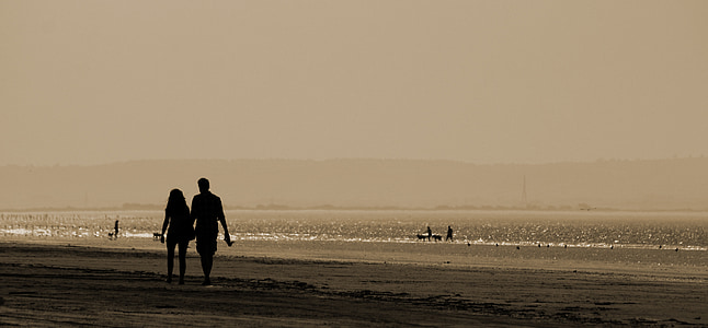 man and woman holding hands while walking near beach