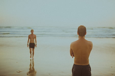 two men wears black shorts stands at seashore