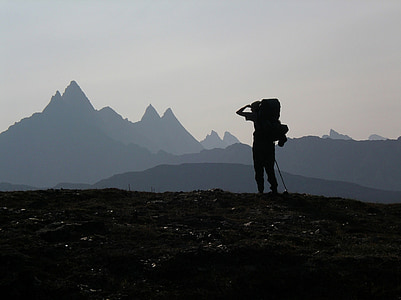 silhouette of person carrying hiking backpack standing near mountain