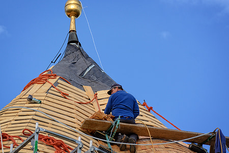 photo of man sitting on plank repairing on roof