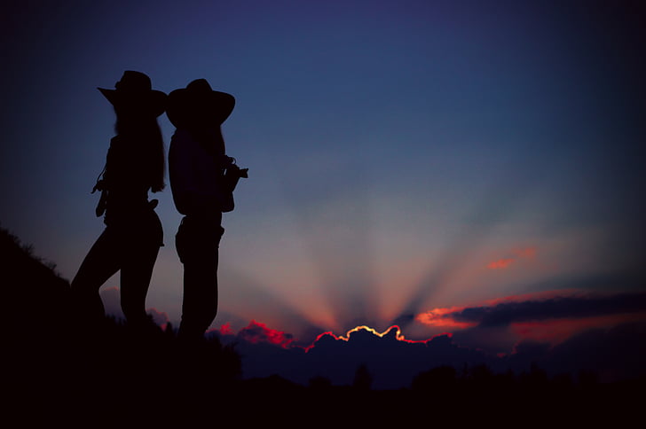 silhouette of two cowgirls standing on a cliff