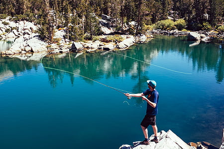 man in blue shirt fishing on lake