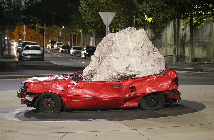 red car squashed by gray stone