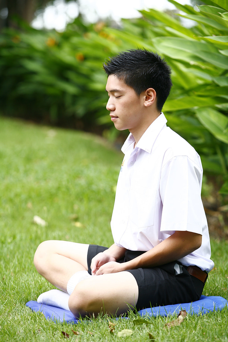 man wearing white shirt meditating on green grass