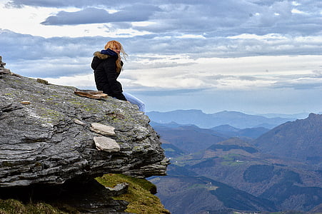 woman wearing parka coat sitting on cliff under blue sky