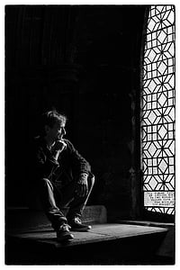 grayscale photography of man sitting on stairs near window
