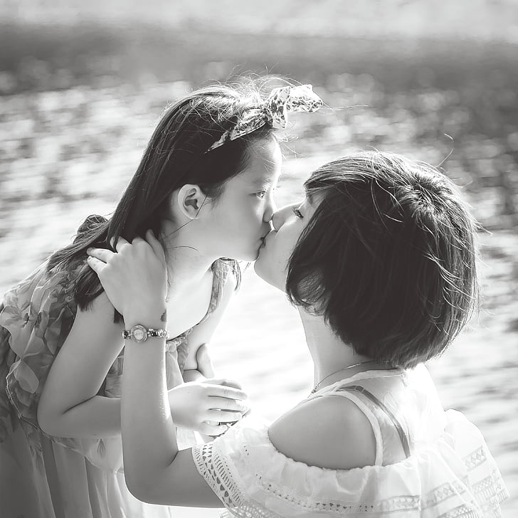 grayscale photo of woman kissing girl