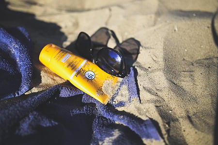 sunglasses and sunblock lotion on sand