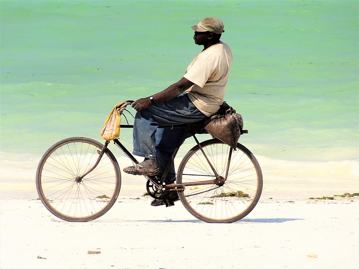 man in beige shirt and blue pants riding bike on shoreline
