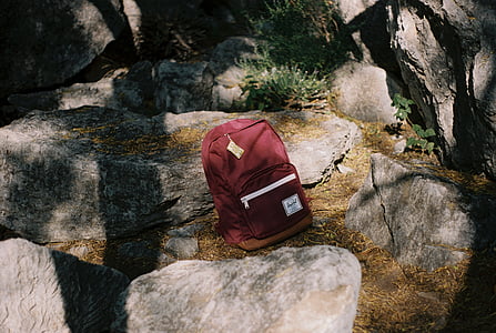 red Herschel backpack placed between gray boulders