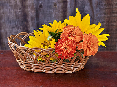sunflowers and red petaled flowers in brown wicker basket