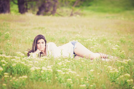 woman wearing white top laying on green grass field