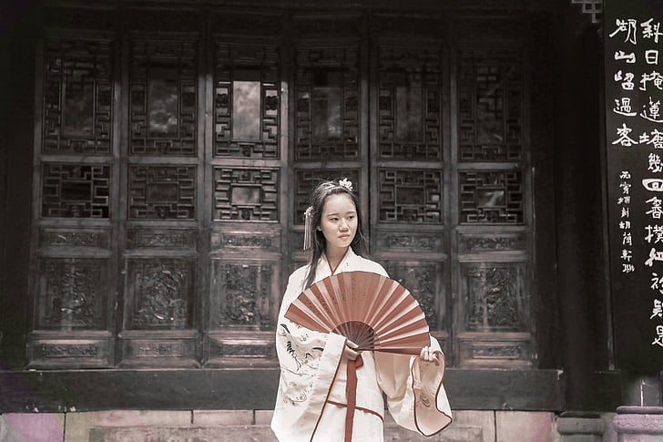 woman wearing white dress holding red fan near black wall