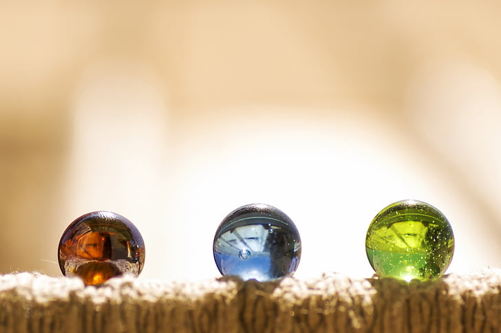 selective focus photography of three assorted-color marbles on brown surface