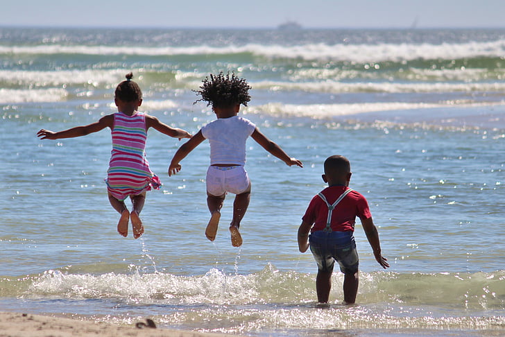three children playing on seashore during daytime