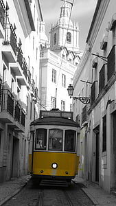 selective color photo of yellow tram between buildings