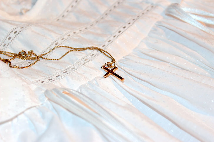 gold-colored cross pendant necklace on white textile \