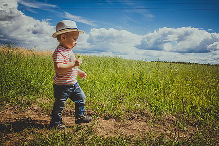 boy standing in middle of grassland under clear sky during daytime