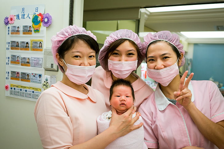 three women wearing pink masks and baby posting for photo