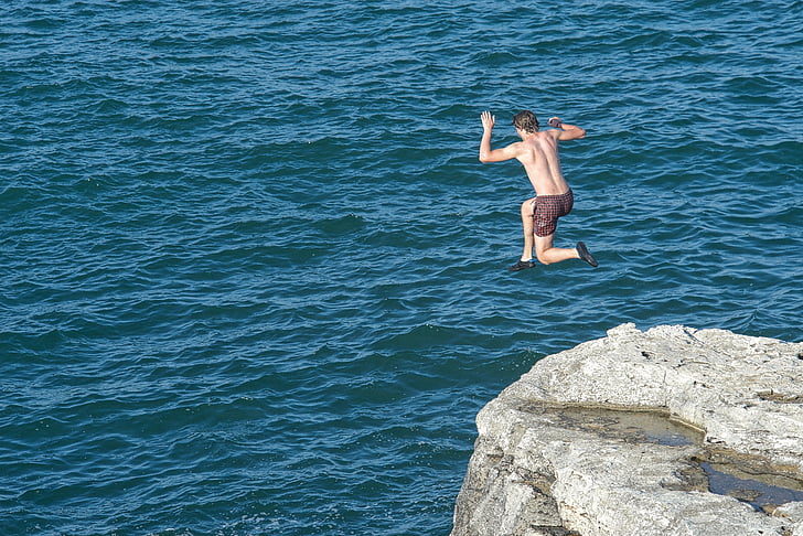 photo of man that jumps on cliff near body of water