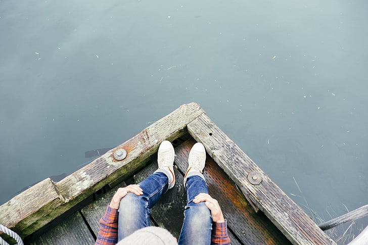 top view photo of person in denim pants sitting on brown wooden dock over body of water