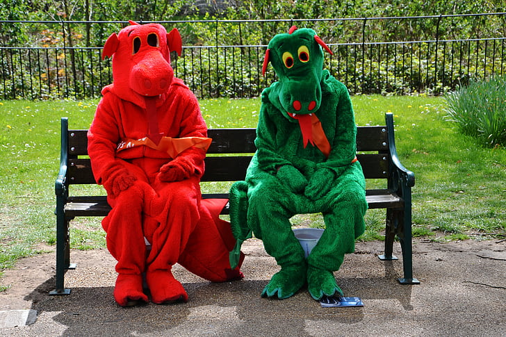 two person wearing red and green dinosaur mascots while sitting on black wooden bench during daytime