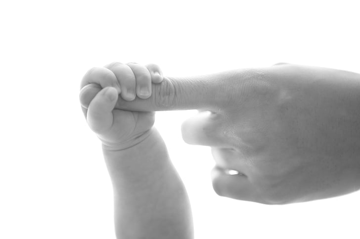 toddler and parent holding finger in greyscale photography