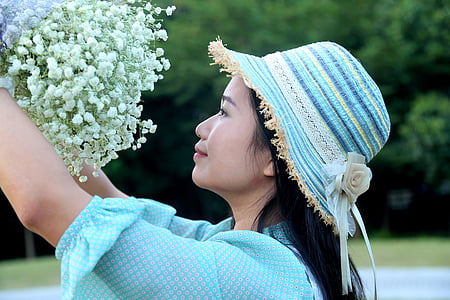 woman wearing teal top and striped hat holding white cluster flowers