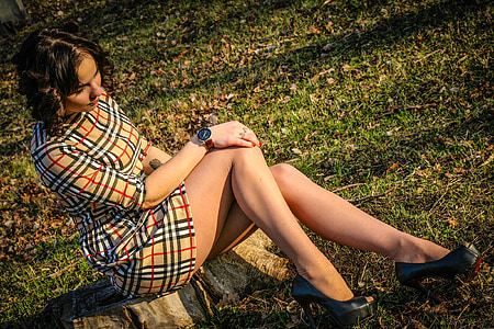 woman wearing brown, red, and white plaid dress sitting down on tree stump