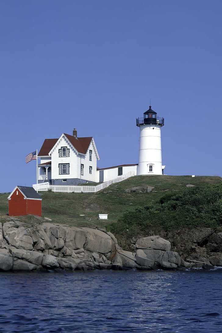 white house and lighthouse on hill near body of water