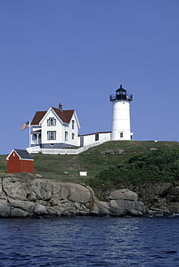 white house and lighthouse on hill near body of water