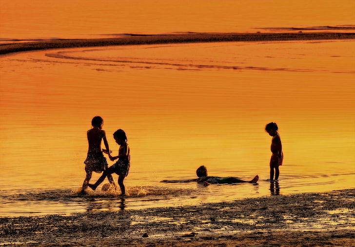 silhouette of four children on seashore during golden hour