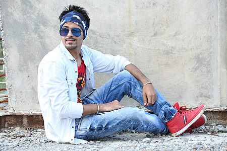 man wearing sunglasses, white sport shirt, blue denim jeans, and red high-top sneakers posing while laying on ground