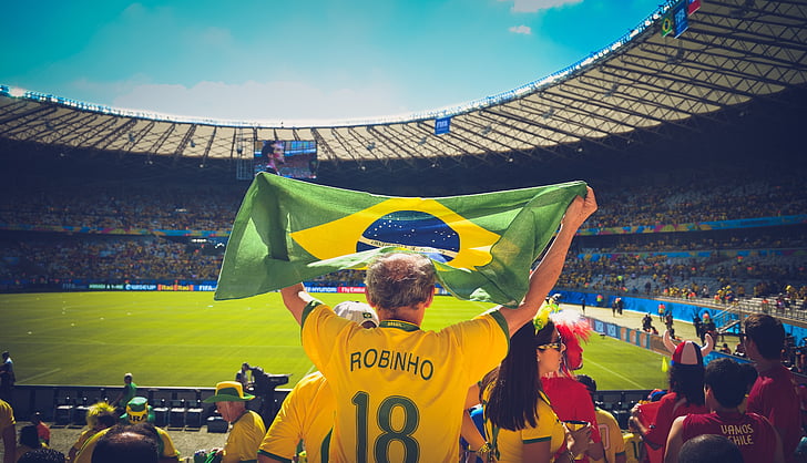 photo of man raising flag of Brazil on sports stadium